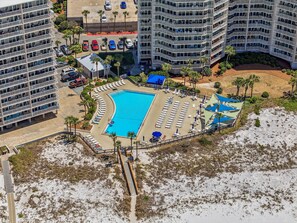 Ein mehrstöckiges Hotel mit Schwimmbad, Liegestühlen und Sonnenschirmen.