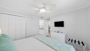 Ein Schlafzimmer mit einem Bett, einem Schminktisch, einem Fernseher und einem Deckenventilator.