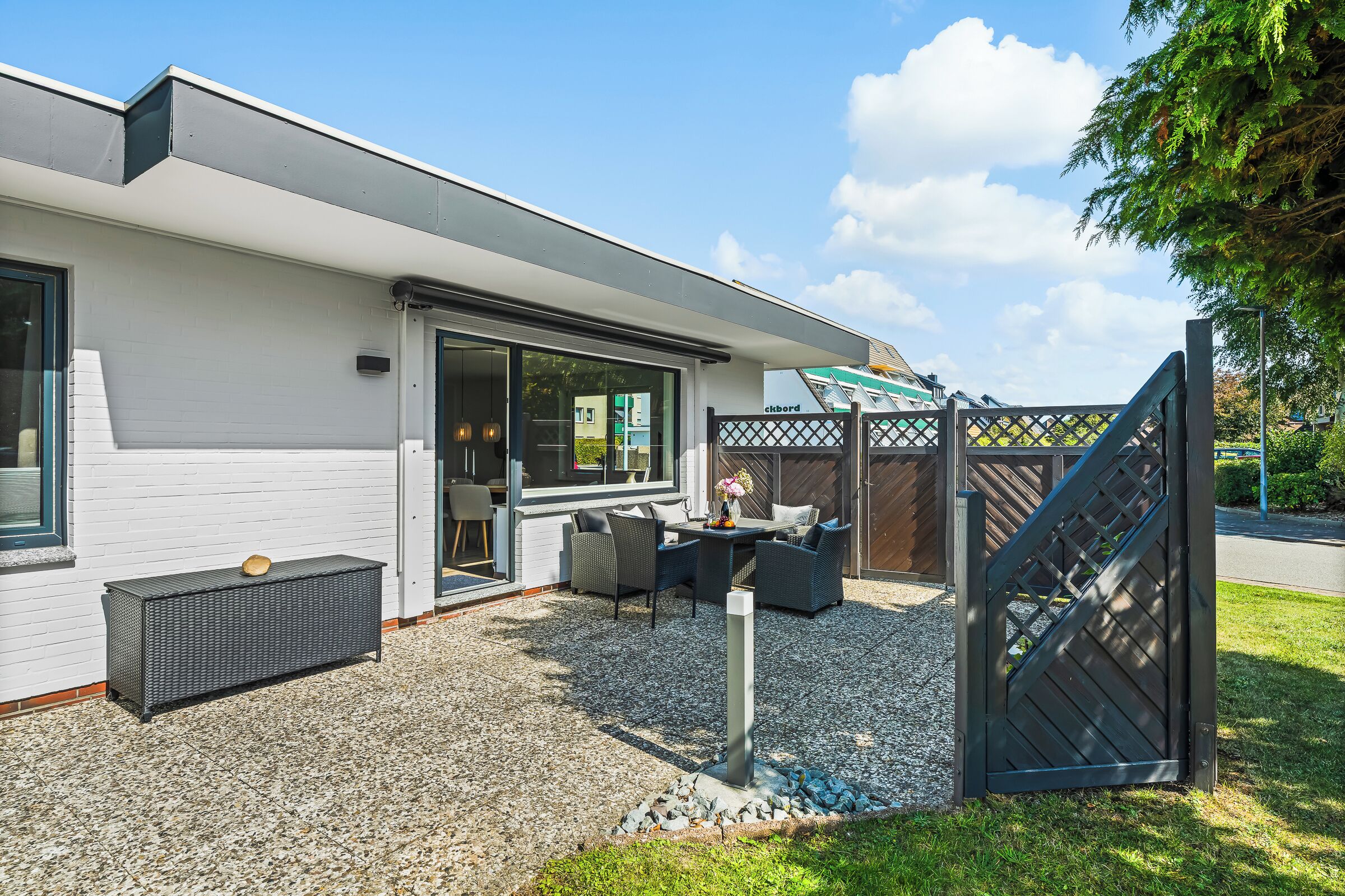 Ein modernes Haus mit einer Terrasse, ausgestattet mit Gartenmöbeln und einem Kiesboden.