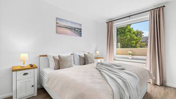 A bedroom with a bed, nightstands, a painting, and a window with curtains.