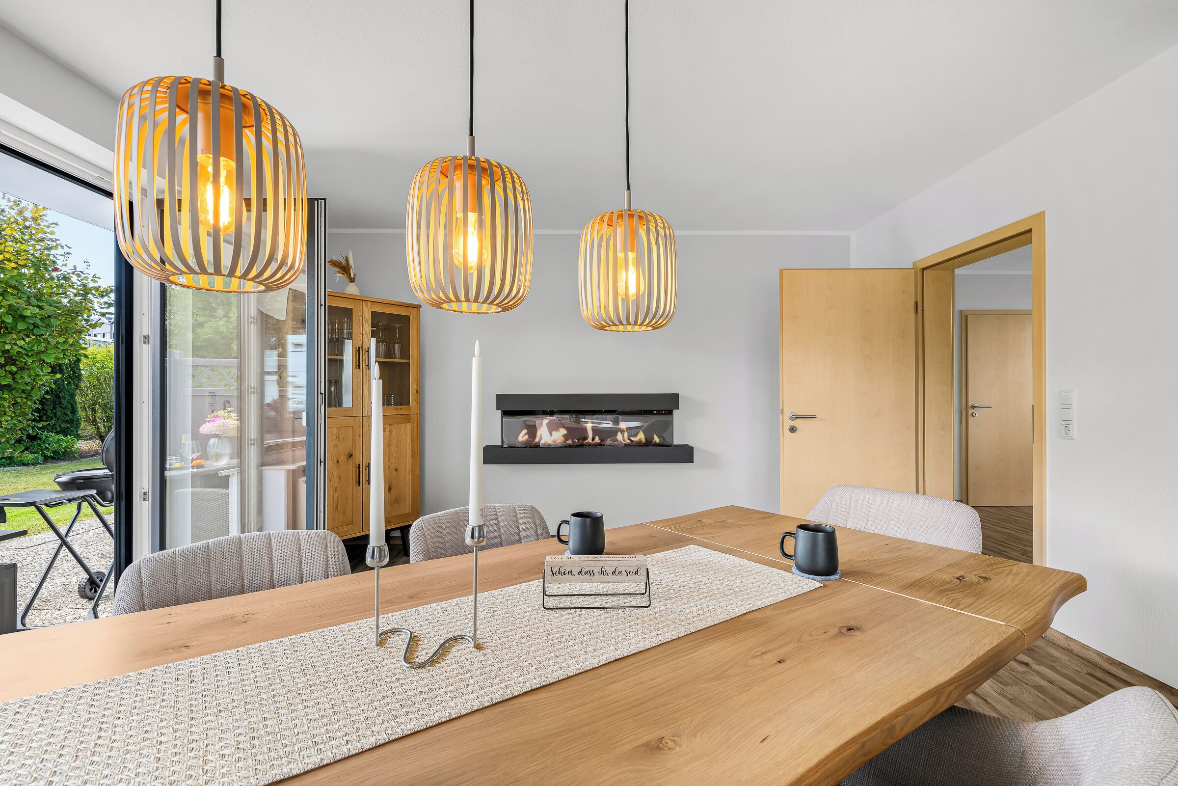 Un comedor moderno con mesa de madera, posavasos tejido y tres lámparas colgantes.