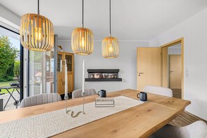 A modern dining area with a wooden table, woven placemat, and three pendant lights. - Blauort Vacation Home in Büsum: Spacious Luxury by the Sea for the Whole Family (Büsum)