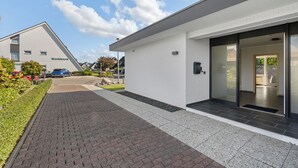A modern building with a white exterior, a paved entrance, and a clear sky. - Blauort Vacation Home in Büsum: Spacious Luxury by the Sea for the Whole Family (Büsum)