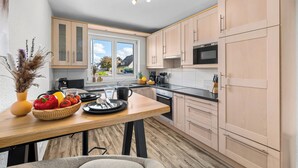 A modern kitchen with wooden cabinets, a dining table with a vase of flowers, and a view of the outside. - Blauort Vacation Home in Büsum: Spacious Luxury by the Sea for the Whole Family (Büsum)
