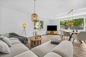 A modern living room with a sofa, coffee table, and dining area. - Blauort Vacation Home in Büsum: Spacious Luxury by the Sea for the Whole Family (Büsum)