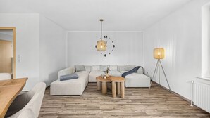 A modern living room with a sectional sofa, a wooden coffee table, and two pendant lights. - Blauort Vacation Home in Büsum: Spacious Luxury by the Sea for the Whole Family (Büsum)