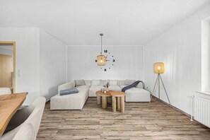 Ein modernes Wohnzimmer mit einem Ecksofa, einem Holztisch und zwei Pendelleuchten.