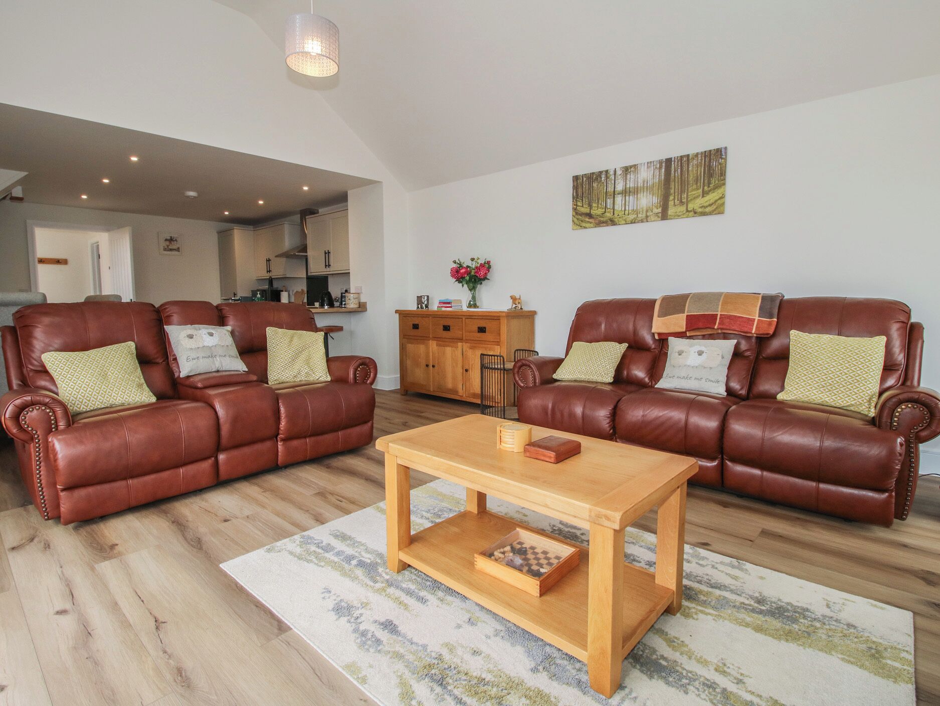 A living room with two brown leather sofas, a wooden coffee table, and a kitchen in the background.