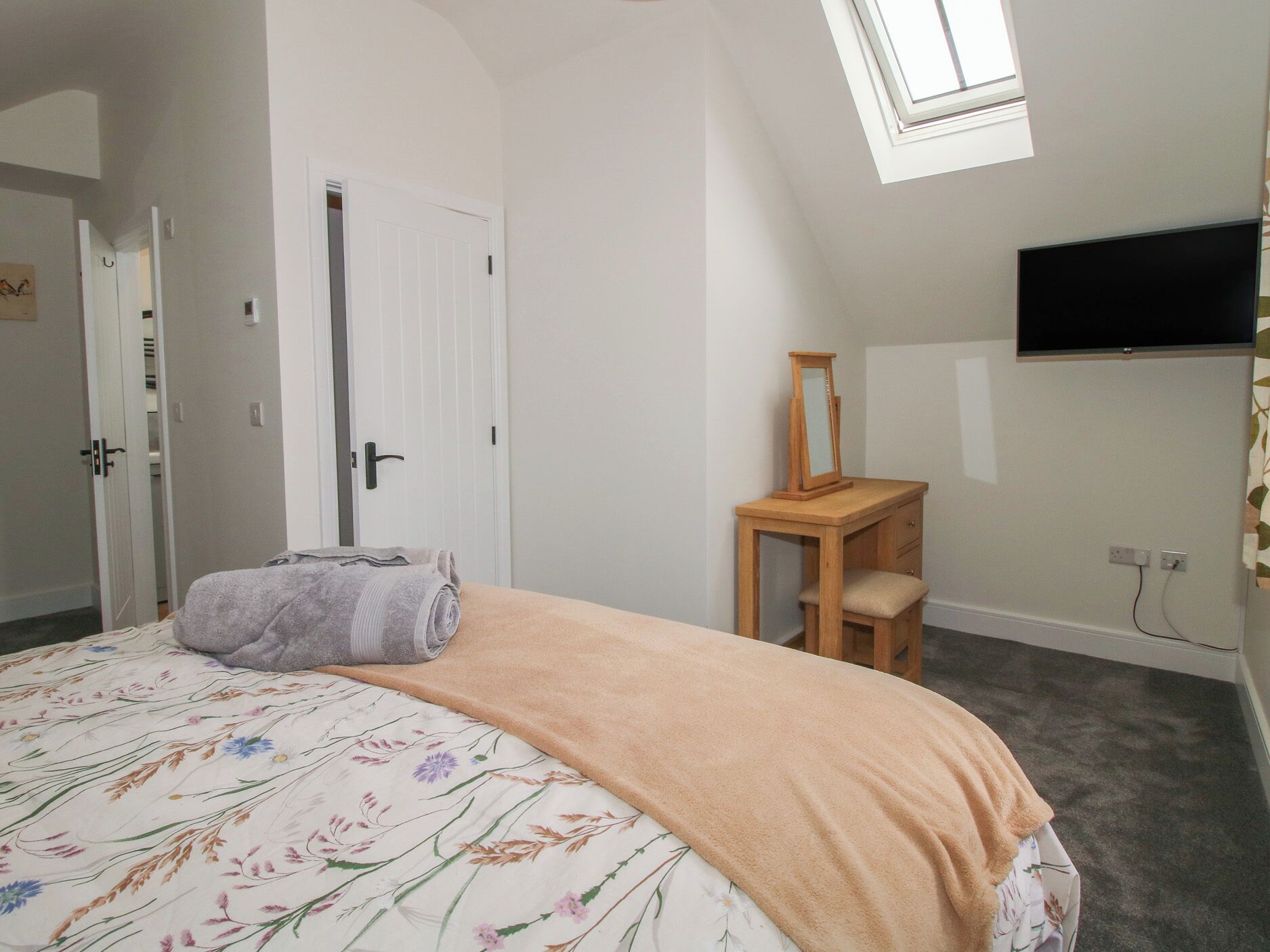 Un dormitorio con cama, mesita de noche, espejo, televisión y puerta.