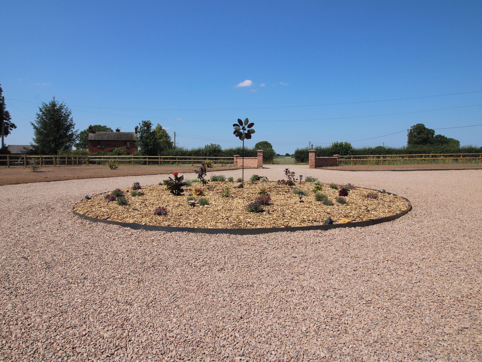 En grusbelagt plads med en rund blomsterbed og en vindmølle i midten.