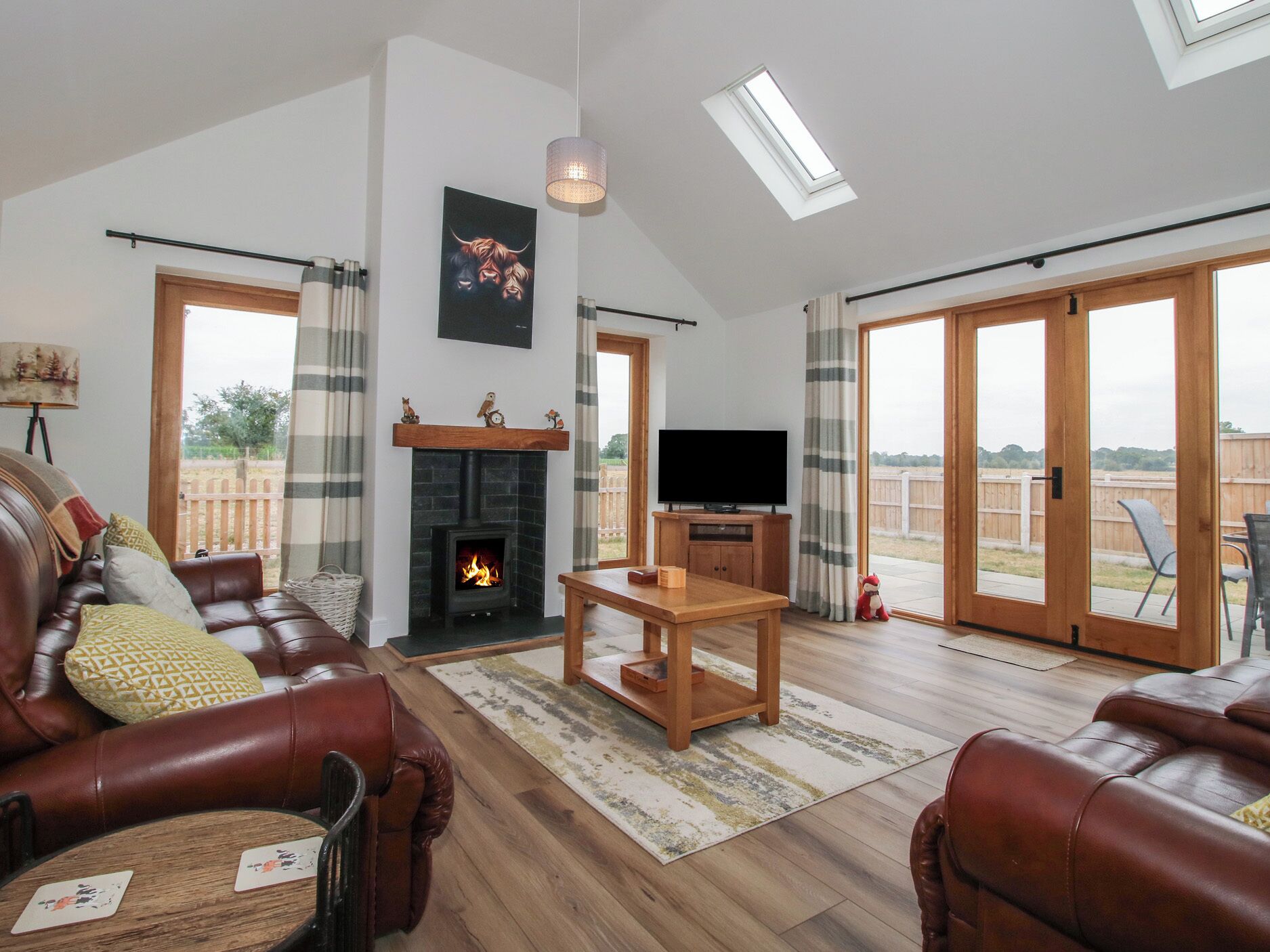 Un salón amplio con chimenea, sofás de cuero, televisión y vistas a través de puertas correderas grandes.