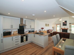 Una cocina moderna con armarios blancos, una isla central y una zona de comedor con mesa de vidrio.