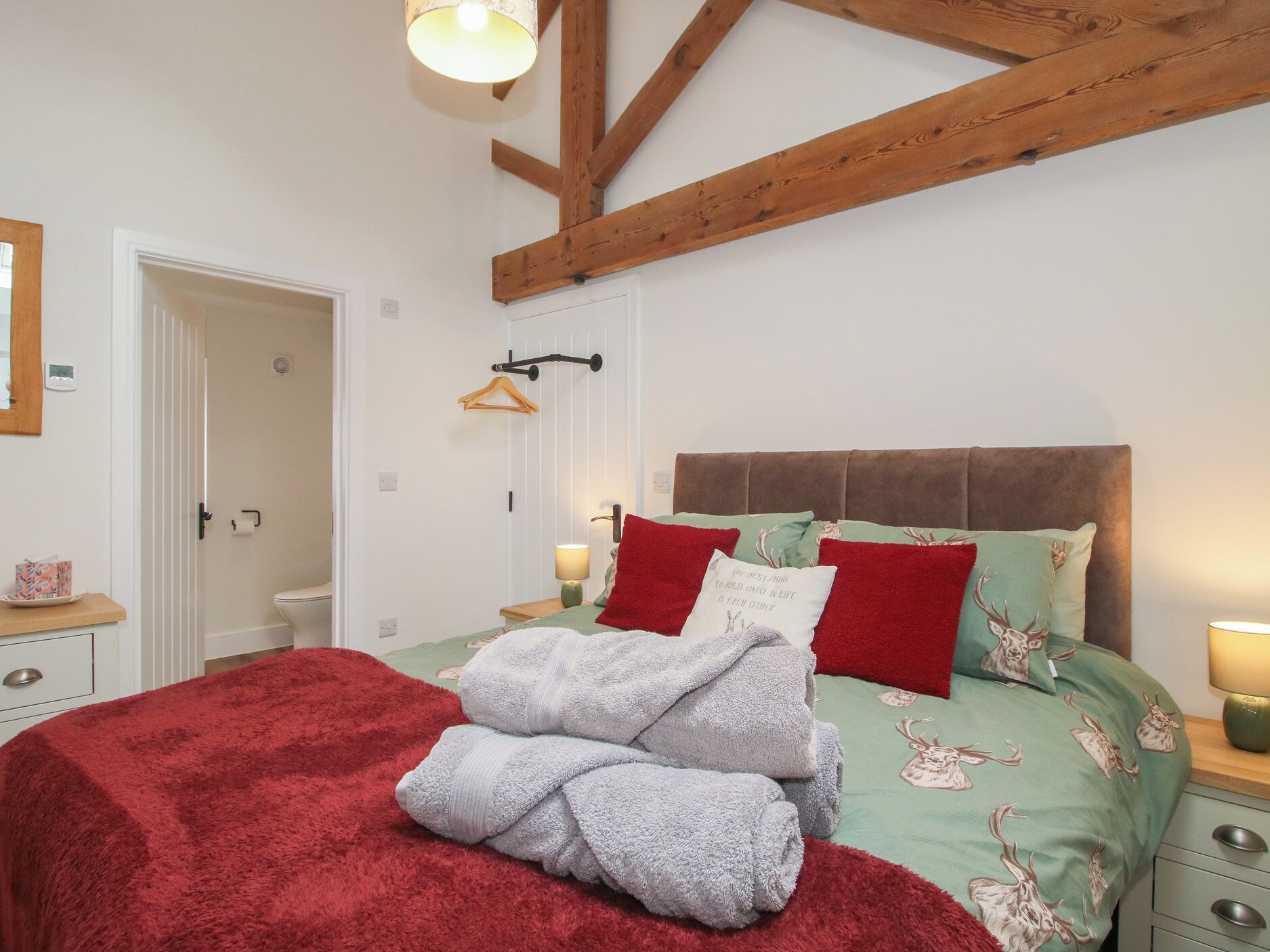 A bedroom with a bed, a nightstand, a bedside table, a hanging light fixture, and a door.