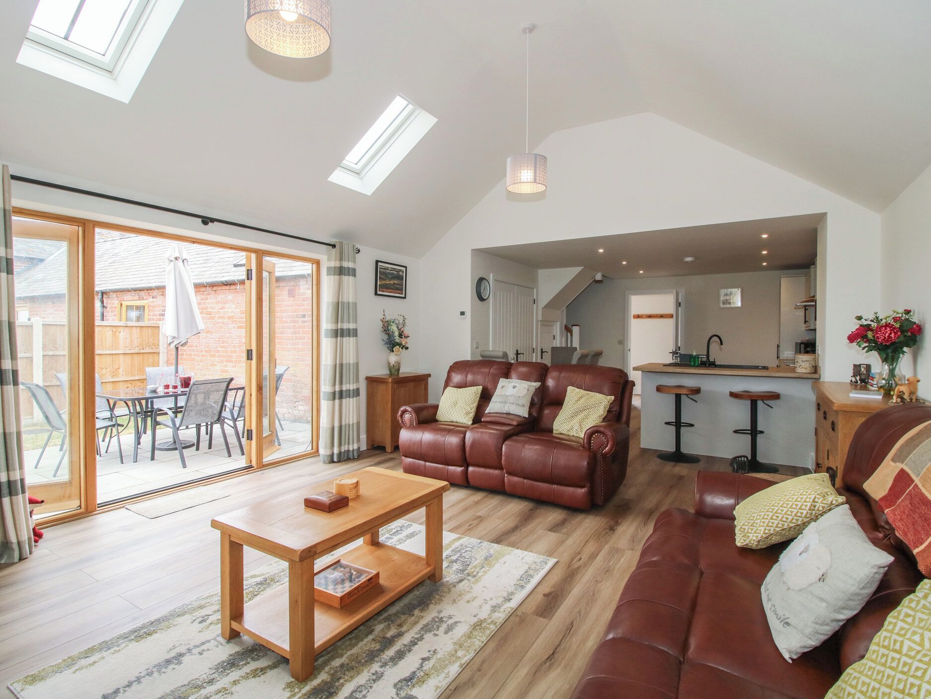 A spacious living area with a brown leather sofa, a wooden coffee table, and a dining table with chairs. There is a sliding glass door leading to an outdoor patio.