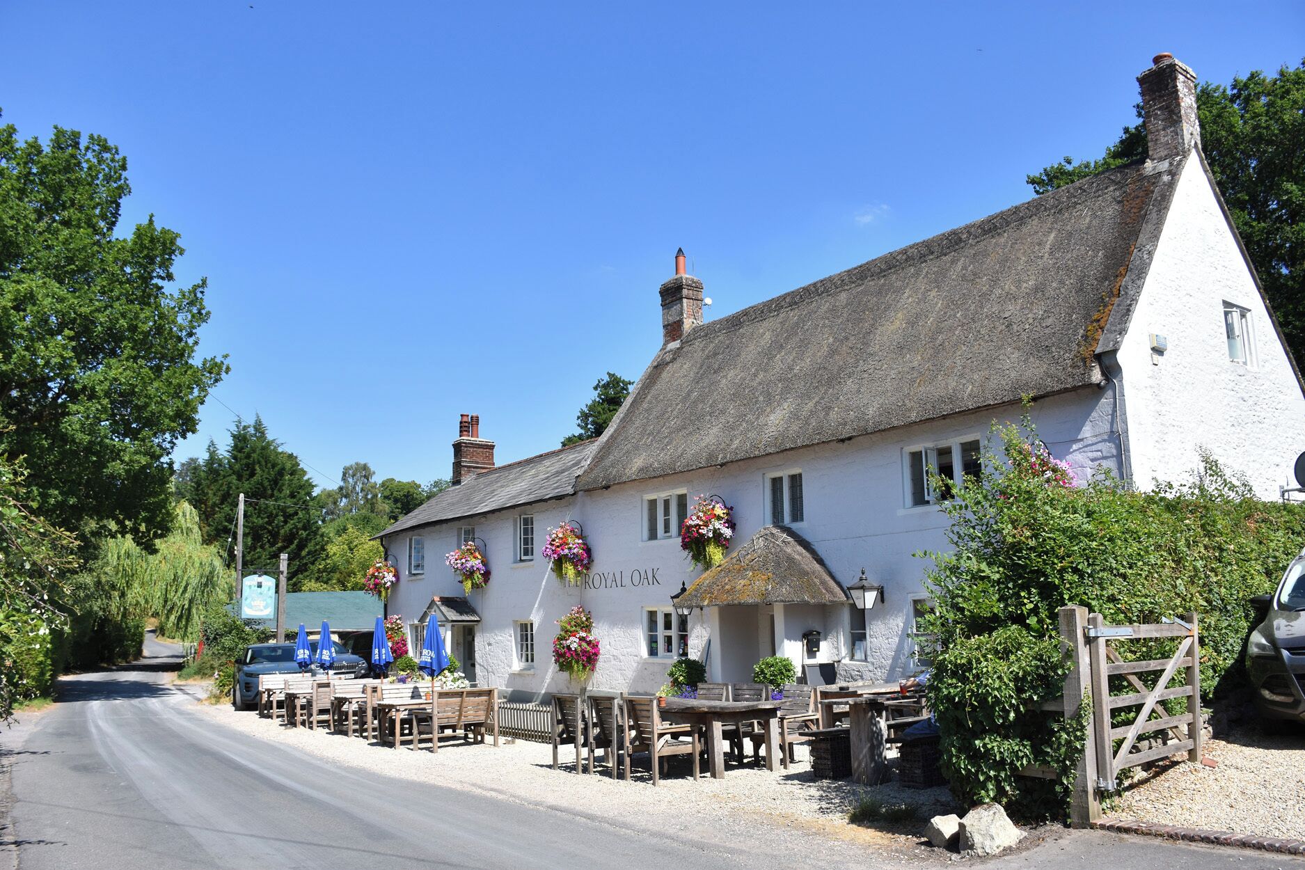 A white building with a thatched roof, named 'ROYAL OAK,' featuring outdoor seating and flower arrangements.