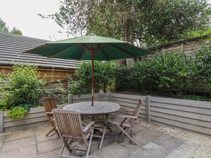 A round wooden table with four chairs and a green umbrella. - Little Orchard (Salisbury)
