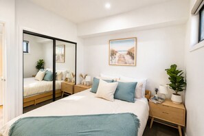A bedroom with a bed, bedside tables, a mirror, a painting, and a potted plant. - The St Kilda Edit - Luxury 2BR Home Minutes to Beach (St Kilda)