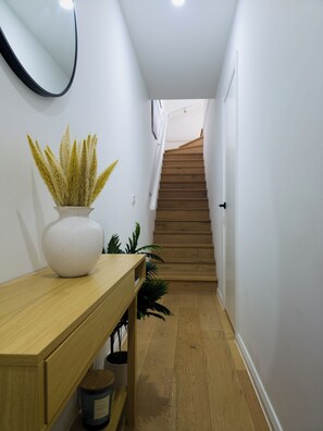 A hallway with a wooden bench, a white vase with plants, and a staircase leading to an upper floor. - The St Kilda Edit - Luxury 2BR Home Minutes to Beach (St Kilda)