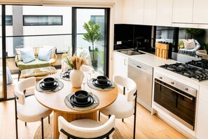 A modern kitchen with a dining area, a view of the city, and a balcony with seating. - The St Kilda Edit - Luxury 2BR Home Minutes to Beach (St Kilda)