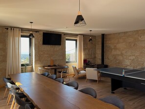 A room with a long wooden table, chairs, a ping pong table, and a TV mounted on the wall. - HOUSE FARMS (Vila Nova de Anha Viana do Castelo)