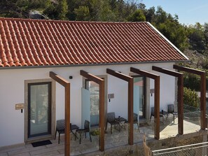 Ein Gebäude mit einem Ziegeldach, einer überdachten Außenbereich-Sitzgelegenheit mit Stühlen und Tischen sowie einer Tür mit der Aufschrift 'SUIETE PERIGONOS'.