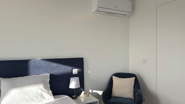 Una camera d'hotel con un letto, una sedia, un comodino, una lampada e un condizionatore d'aria.