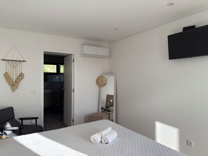 Una habitació d'hotel amb un llit, una cadira, una televisió i una porta que dóna a un bany.