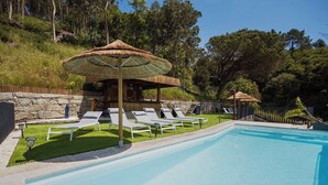 Una piscina con lettini e ombrelloni, circondata da un muro in pietra e vegetazione.