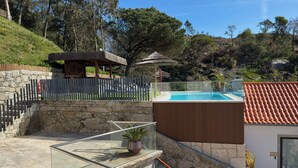 Zona piscina con parete in pietra, terrazza in legno e balaustra in vetro.