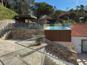 A pool area with a stone wall, a wooden deck, and a glass balustrade.