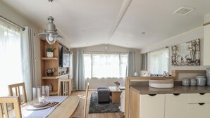 Uma cozinha moderna com armários de madeira, uma área de jantar com mesa e cadeiras, e uma janela grande com cortinas.