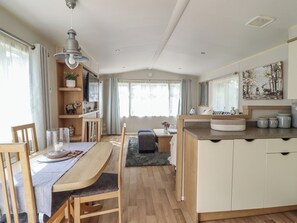 A modern kitchen with wooden cabinetry, a dining area with a table and chairs, and a large window with curtains. - Plot 13A (Ruthin)