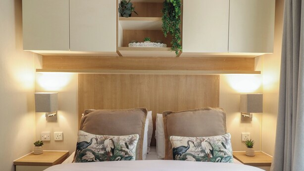 Quarto de hotel com cama, duas mesinhas de cabeceira, luminárias fixadas na parede e uma estante com objetos decorativos.