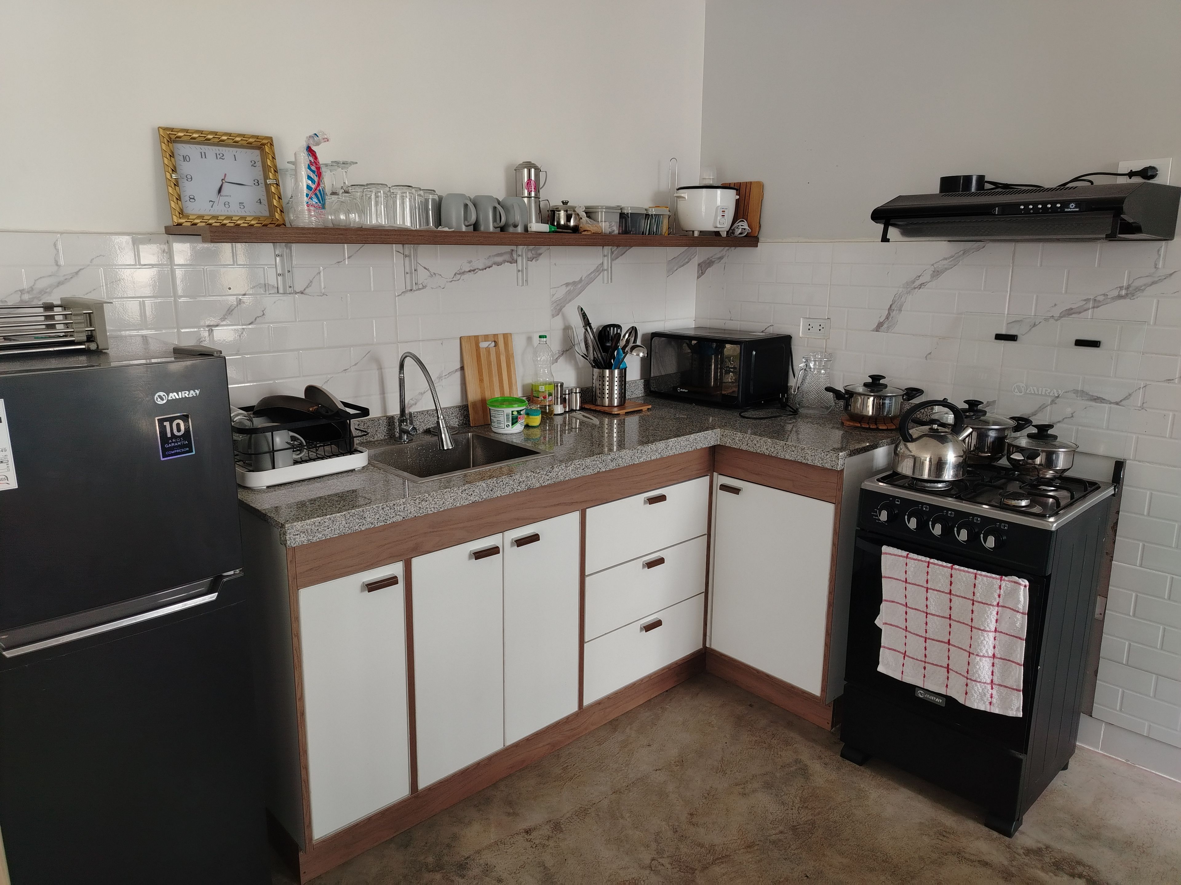 A kitchen with a refrigerator, stove, microwave, sink, and various kitchen items on the countertop.