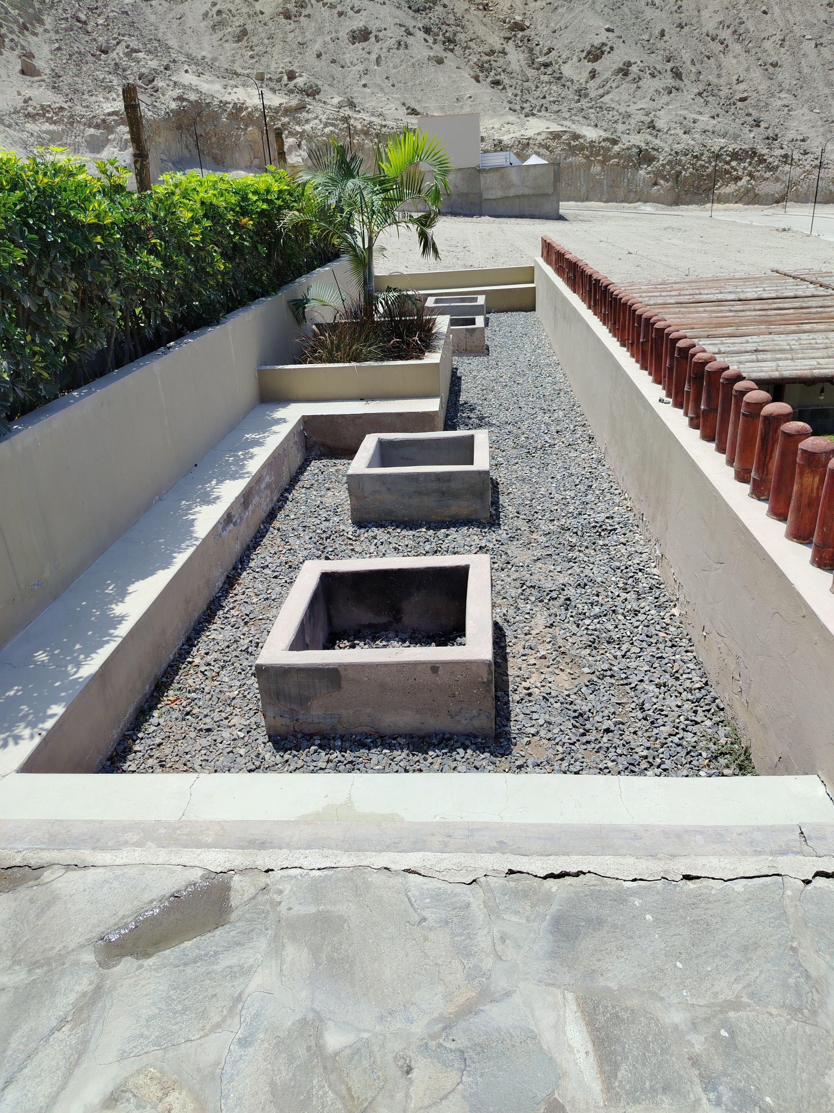 Un chemin bordé de jardinières en béton et recouvert de gravier.