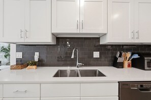 A modern kitchen with white cabinets, a stainless steel sink, and a black tiled backsplash. - Lake vista condo #201 - newly remodeled (Kissimmee)