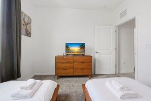 Ein Hotelzimmer mit zwei Betten, einem Holzschrank, einem Sonnenuntergangsbild und einer weißen Tür.