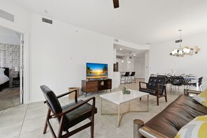 Un salon moderne doté d’un téléviseur à écran plat, de canapés en cuir, d’un coin repas avec une table et des chaises, et d’une cuisine en arrière-plan.