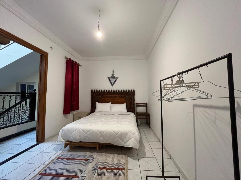 Un dormitorio con cama, lámpara colgante, perchero en la pared y vistas a un balcón.