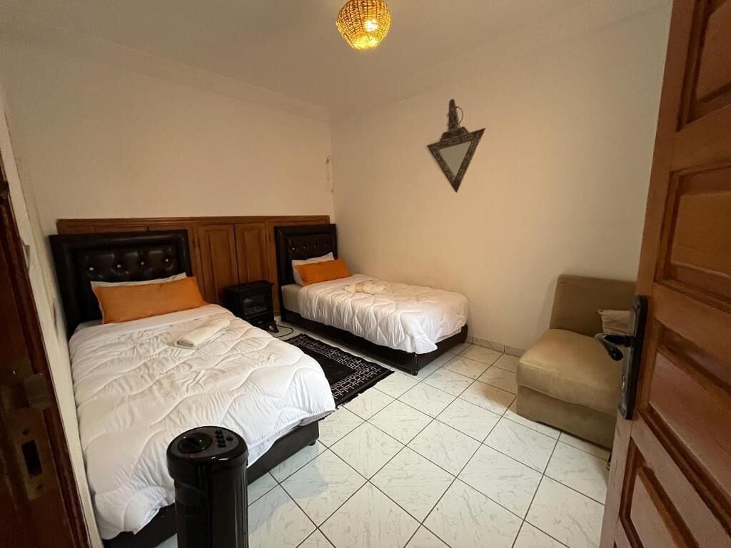 A bedroom with two beds, a bedside table, a lamp, and a wall-mounted decoration.