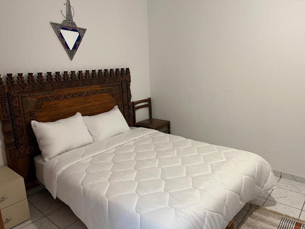 A bed with a wooden headboard, a bedside table, and a wall-mounted decorative item.