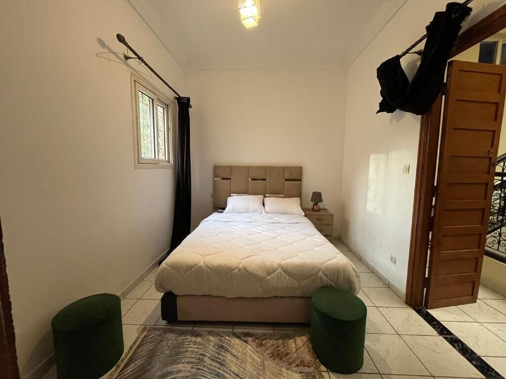 A bedroom with a bed, bedside table, lamp, and a window with curtains.