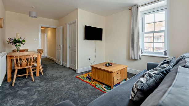 En moderne stue med et fladskærms-tv, et træ sofabord, en sofa og et spiseområde med stole og et bord.