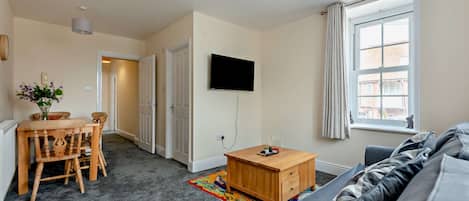 Una sala de estar moderna con un televisor de pantalla plana, una mesa de centro de madera, un sofá y un área de comedor con sillas y una mesa.