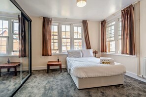 Ein Schlafzimmer mit einem großen Bett, einem Nachttisch, einem Spiegel und einem Fenster mit Vorhängen.