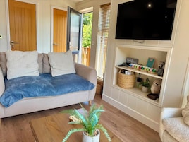 Una sala de estar acogedora con un sofá, un televisor de pantalla plana, un estante con objetos decorativos y una puerta que da al exterior.