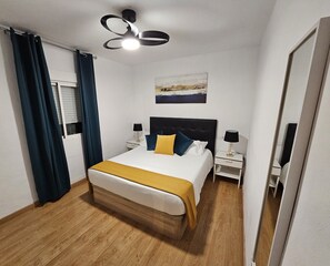 Une chambre à coucher avec un lit, des tables de chevet, un luminaire au plafond, un tableau et un miroir.