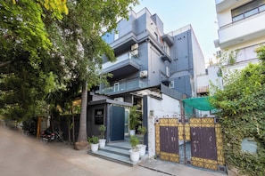 Un edificio moderno de dos pisos con balcón, entrada con reja y plantas en macetas.