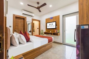 Habitación de hotel con cama, ventilador de techo, aire acondicionado, televisor montado en la pared y refrigerador.