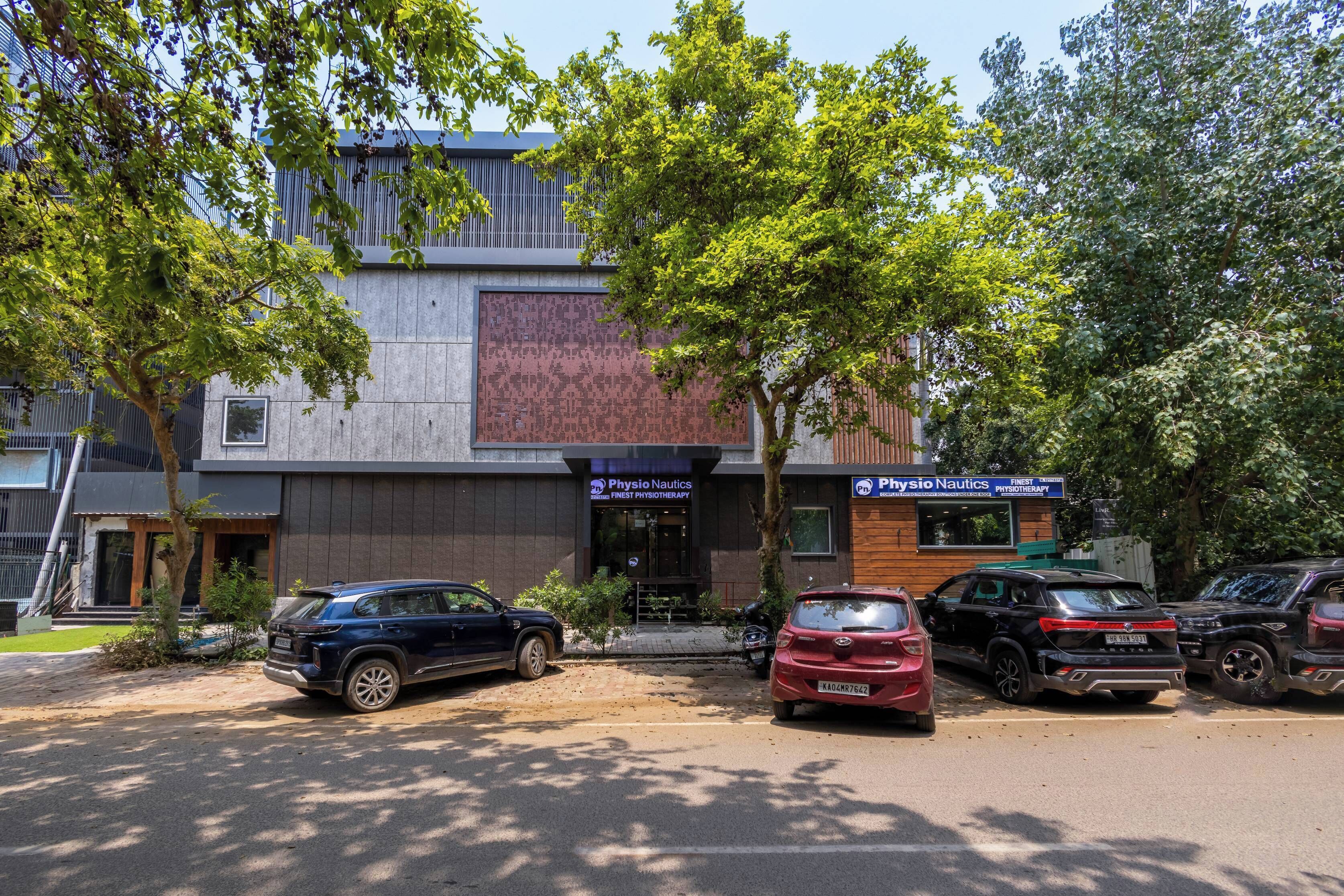 A building with a modern facade, a Physio Nautics sign, and several parked cars.